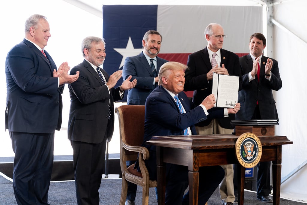 A man seated at a desk proudly holds up a signed document.