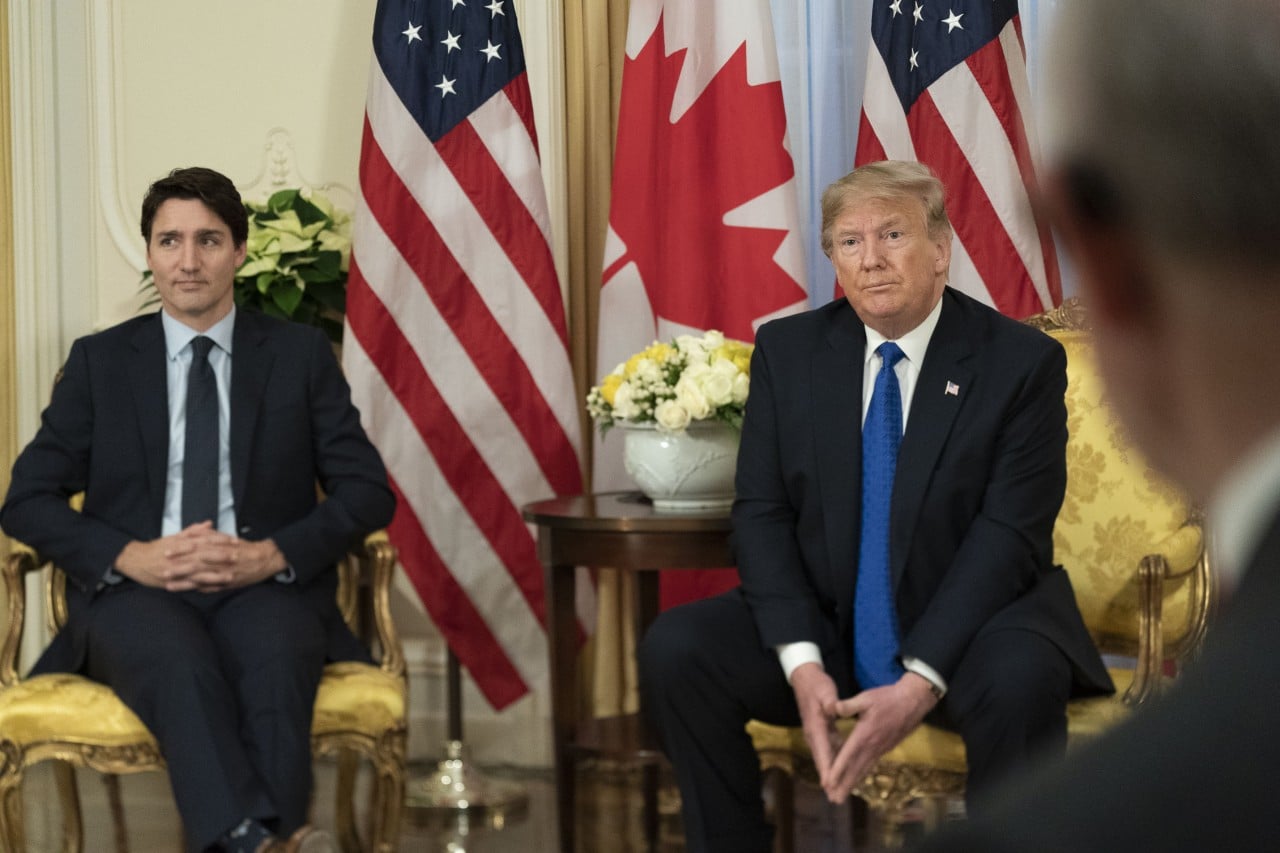 Two men sit beside each other with American and Canadian flags in the background.