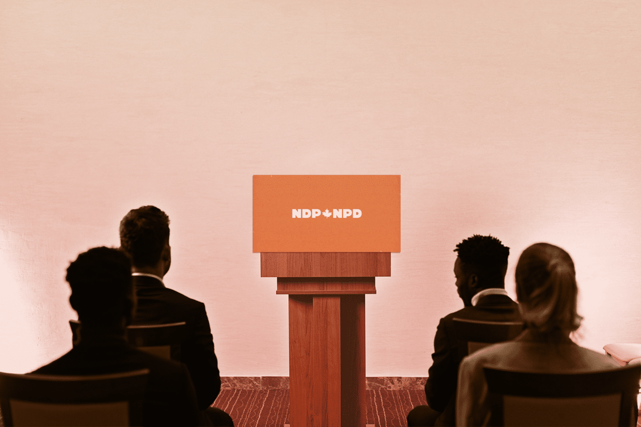 Onlookers sit in front of empty NDP podium